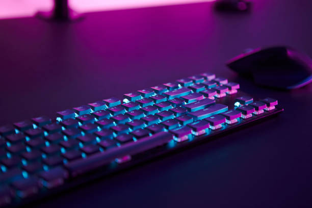 istock Computer mouse and illuminated keyboard laying on desk. Pink light in background. 1335367995