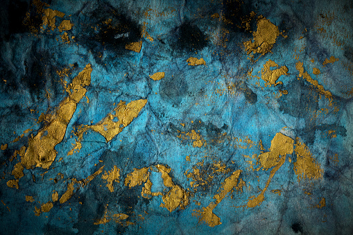 Abstract grunge hand painted gold paint stroke texture on a blue teal paper background