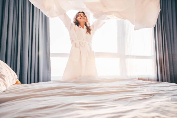 Woman making bed in the sunny morning. Woman doing morning routine. stock photo