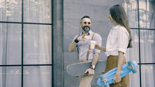 Couple walking together holding takeaway coffee cup and skateboard stock photo