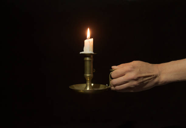 istock Decorative copper candlestick with burning candles in a female hand on a black background. Close-up 1335378268