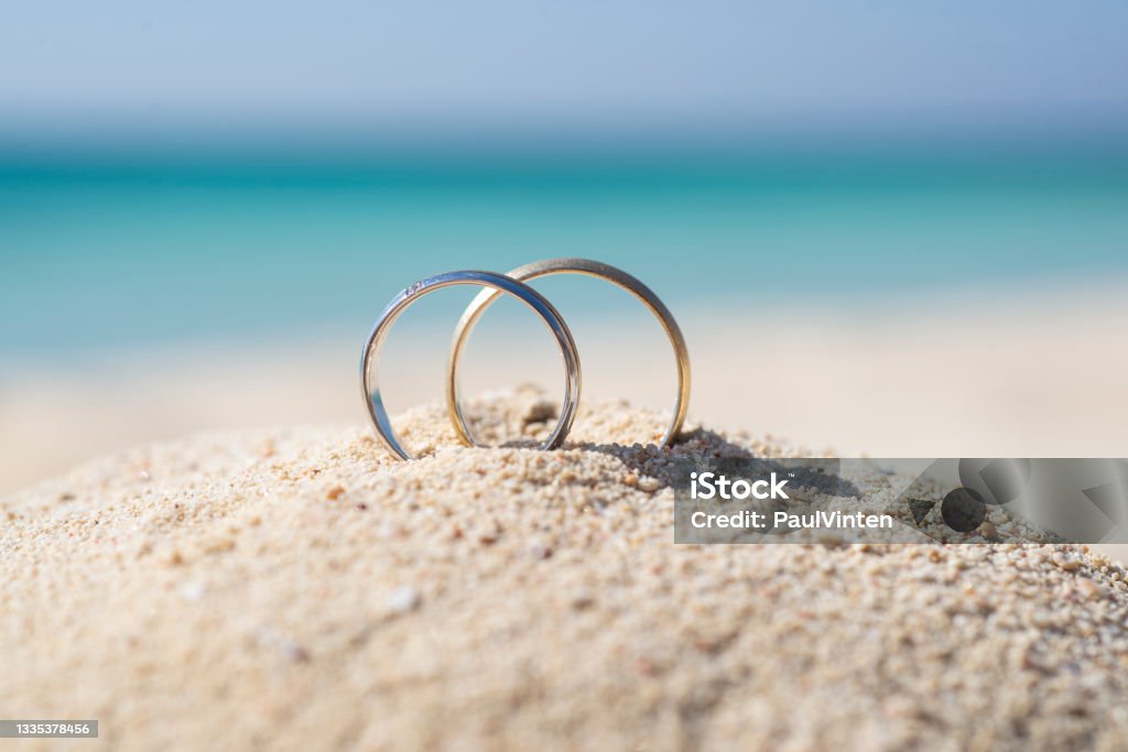 Pair wedding rings in sand on tropical beach Pair of gold wedding ring bands jewelry in sand on tropical desert island beach during summer with blue ocean background Wedding Stock Photo