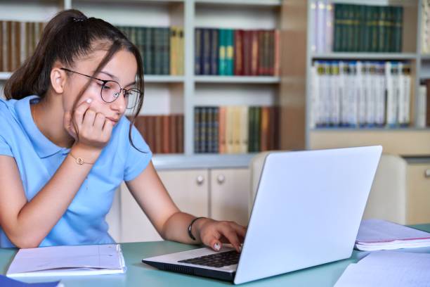 niña adolescente de 14, 15 años con gafas estudia en biblioteca, usando laptop. - 13 14 years teenager teenagers only female fotografías e imágenes de stock