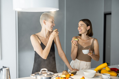 Lesbian couple have a breakfast together with avocado sandwich and coffee at modern kitchen. Homosexual relations and healthy eating in a comfortable home