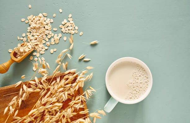 Oat milk in a glass and mug on a blue background. Flakes and ears for oatmeal and granola on a wooden plate. stock photo