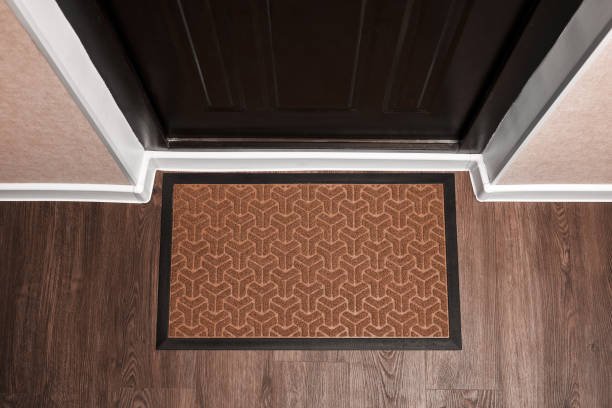 Blank doormat before the dark door in the hall. Top view of mat on wooden floor. Mockup for your design stock photo