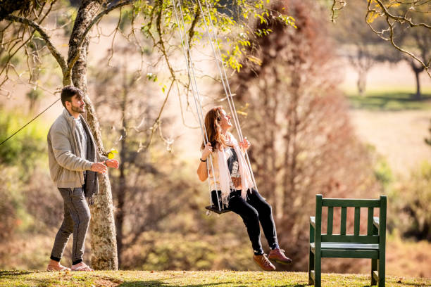 istock Man pushing his partner on swing at park 1335394102