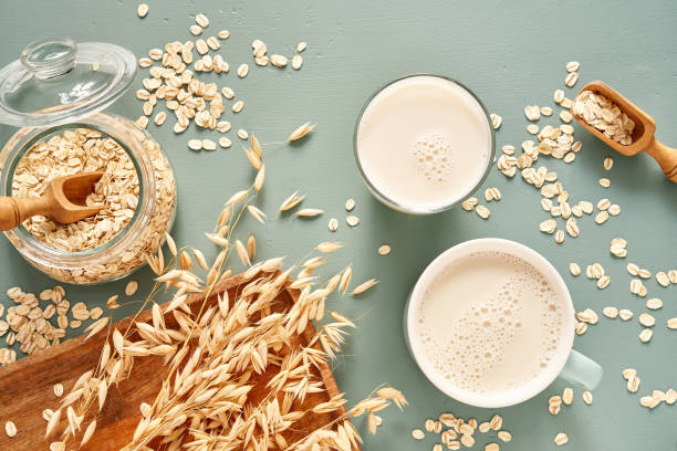 Oat milk in a glass and mug on a blue background. Flakes and ears for oatmeal and granola on a wooden plate. Oat milk in a glass and mug on a blue background. Flakes and ears for oatmeal and granola on a wooden plate. granola photos stock pictures, royalty-free photos & images