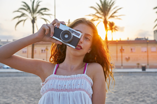 Teen girl with retro photo camera at sunset as a photographer