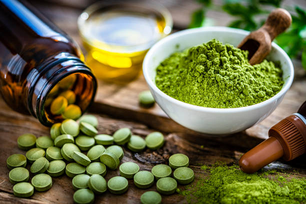 Moringa oleifera powder and pills on rustic table Nutritional supplement: Moringa powder in a white bowl and Moringa capsules spilling out a bottle shot on rustic wooden table. High resolution 42Mp studio digital capture taken with Sony A7rII and Sony FE 90mm f2.8 macro G OSS lens green tea powder stock pictures, royalty-free photos & images