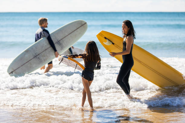 la famiglia australiana si dirige in acqua per un surf - surfing new south wales beach australia foto e immagini stock