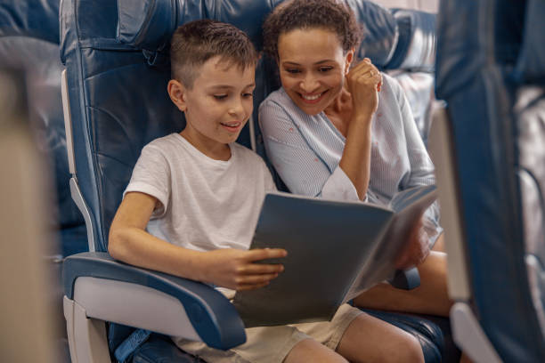 istock Boy, kid on board holding a book and looking trough it together with his mom during flight. Cabin crew providing service to family in airplane 1335402624