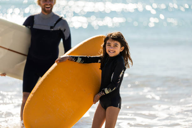 Surfing dad and daughter carry their boards from the surf