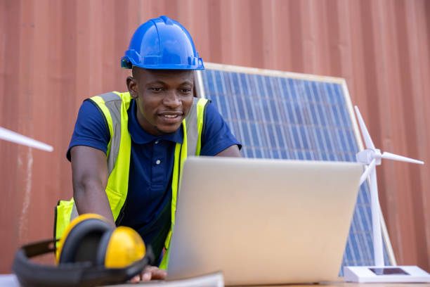 ingénieur afro-américain et électricien caucasien portant un casque de sécurité bleu travaillant sur un ordinateur portable sur un lieu de travail concept d’énergie alternative propre et verte. - production dénergie photos et images de collection