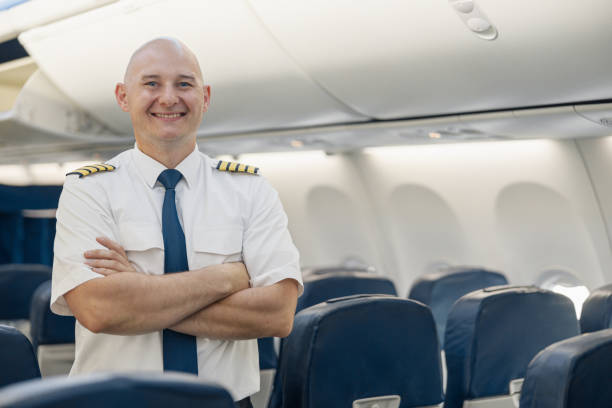 istock Cheerful male pilot in uniform keeping arms crossed and smiling at camera while standing inside of the airplane 1335408653
