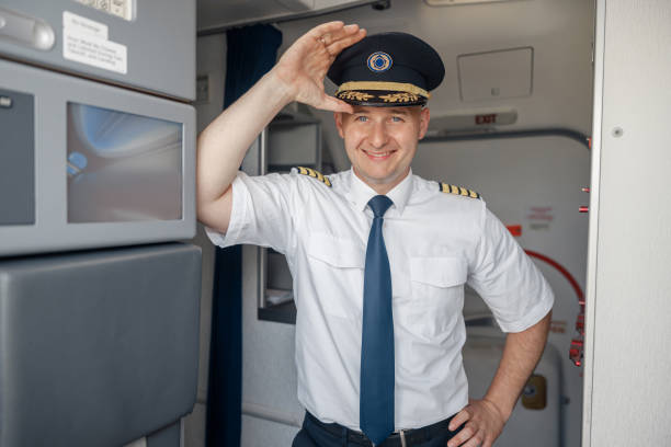istock Joyful male pilot in uniform and hat smiling at camera while standing inside of the airplane 1335408659