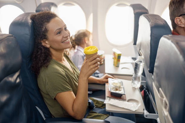 幸せな女性の乗客はコーヒーを飲み、女性客室乗務員が機内で昼食を提供しながら笑顔 - vehicle interior 写真 ストックフォトと画像