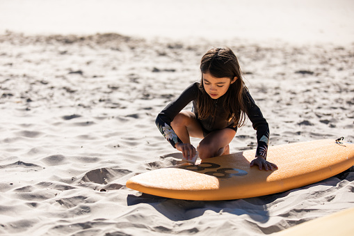 Mixed race girl waxes her surfboard on the beach