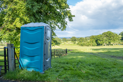 A single plastic blue portable toilet in a field at an outdoor equestrian event in England