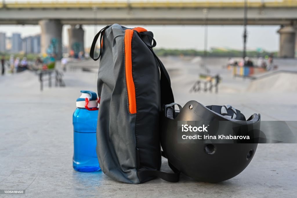 skateboard helmet, backpack and blue bottle of water on concrete on skate park and bridge background Active Lifestyle Stock Photo