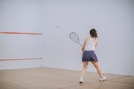 rear view asian chinese teenage girl playing squash alone in the court