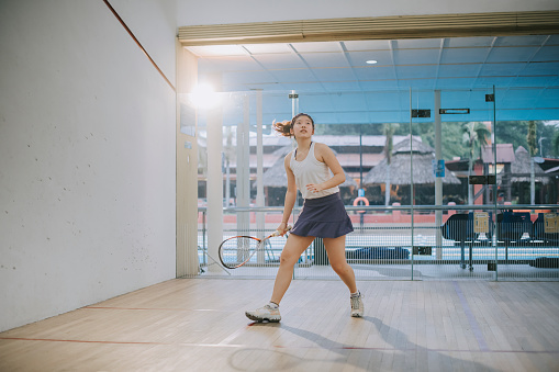 asian chinese teenage girl playing squash alone in the court