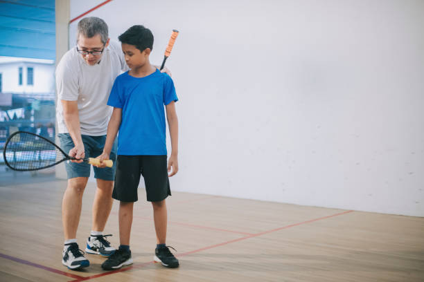 Asian squash coach guiding teaching his student squash showing them in the game