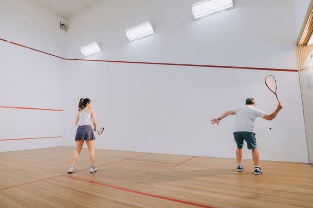 vue de côté entraîneur de squash asiatique père guidant l’enseignement du sport de squash à sa fille s’entraînant ensemble sur un terrain de squash - racketball racket ball court photos et images de collection