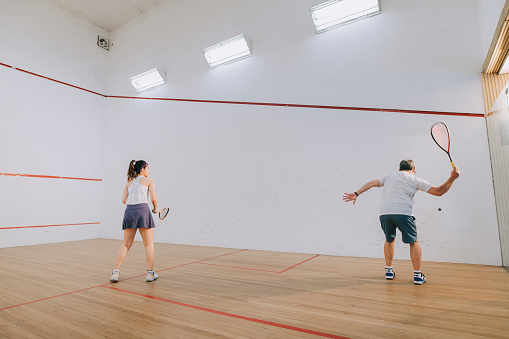 Asian squash coach father guiding teaching his daughter squash sport practicing together in squash court