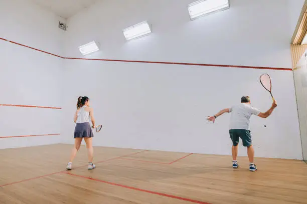Photo of side view Asian squash coach father guiding teaching his daughter squash sport practicing together in squash court