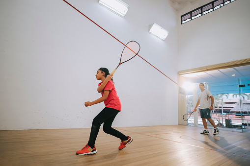 young Asian indian female squash player practicing with guidance from her coach