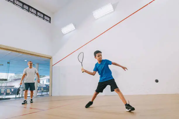 Photo of young Asian malay male squash player practicing with guidance from his coach