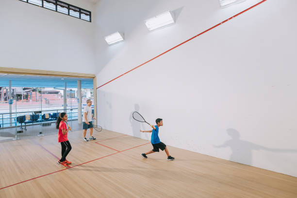 breitschuss asiatischer squashtrainer übt mit seinen 2 schülern auf squashplatz zusammen und zeigt aufschlagmethode - racket ball indoors competition stock-fotos und bilder