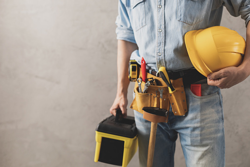 Worker man holding construction helmet and toolbox near wall. Male hand and tools for house room renovation. Home renovation concept