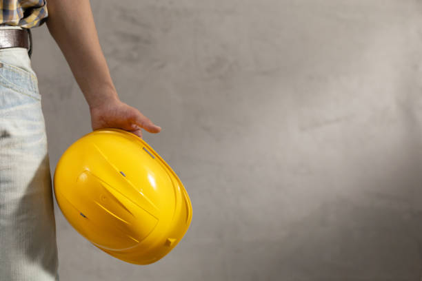 istock Worker man holding construction helmet tool near concrete or cement wall. Male hand and work cap for house room renovation 1335420641