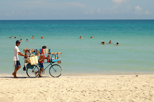 Cuba. August 09, 2019. Varadero: boy walking with his beach stall of necklaces and bags on the shore of the beach