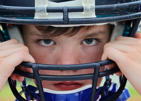 Full frame portrait of young athlete with determination in his eyes donning football helmet on game day.