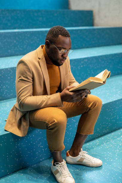 istock Contemporary African student with open book reading on blue staircase 1335438717