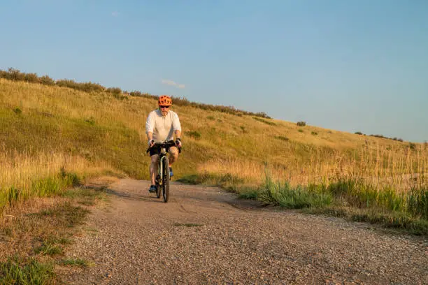 senior male cyclist is riding a touring bike on a gravel trail at Colorado foothills, summer scenery