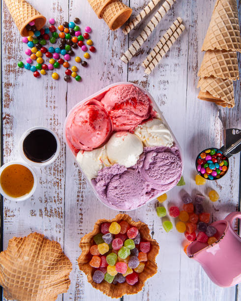 istock Three flavors of ice cream in a delivery container, making a composition with several cones and colored gums. Top view 1335446710