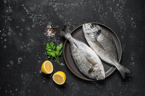 Fresh raw sea dorado fish with spices and lemon on a black stone background. Top view, flat lay. Fresh raw sea dorado fish with spices and lemon on a black stone background. Top view, flat lay catch of fish stock pictures, royalty-free photos & images