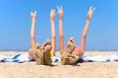 The concept of a wonderful seaside holiday. Children's feet with adhered sand against the background of the sea and raised hands.