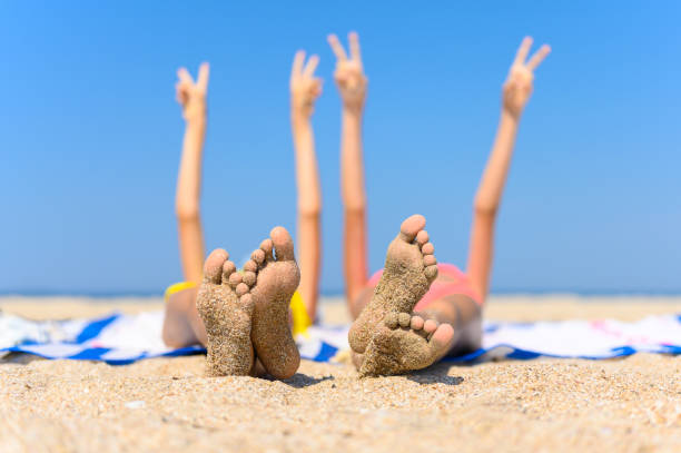 The concept of a wonderful seaside holiday. Children's feet with adhered sand against the background of the sea and raised hands. The concept of a wonderful seaside holiday. Children's feet with adhered sand against the background of the sea and raised hands. Selective focus and shallow depth of field. beach holiday stock pictures, royalty-free photos & images