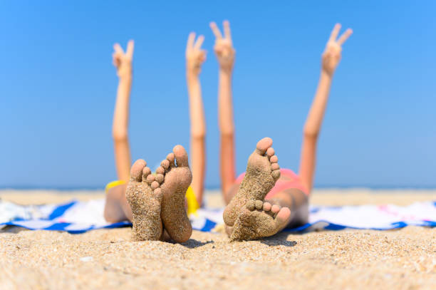 o conceito de um maravilhoso feriado à beira-mar. pés de crianças com areia aderida no fundo do mar e mãos levantadas. - summer beach vacations sand - fotografias e filmes do acervo