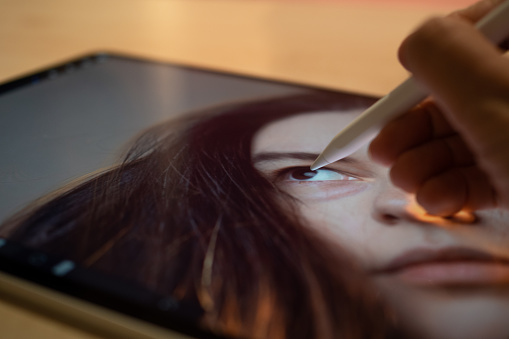 Photo retouching and drawing with a stylus on the screen of a modern graphic tablet. The author's hand edits a photo portrait on a tablet, mobile photo editors