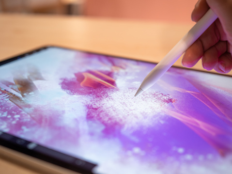 Drawing on a graphic tablet, the artist's hand draws an abstract pattern on the display using a stylus, Digital art in mobile applications