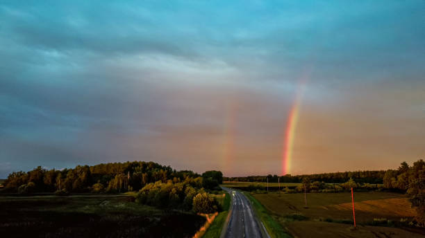 istock Double Rainbow Over Forest and Wheat Field. Dark Thunderstorm Clouds and Rainbow Over Rural Highway Road Landscape. Camera Moves Backward. Aerial Shot 1335468320