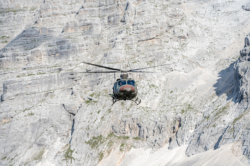 Rescue helicopter flying against high rocky mountain and blue sky.