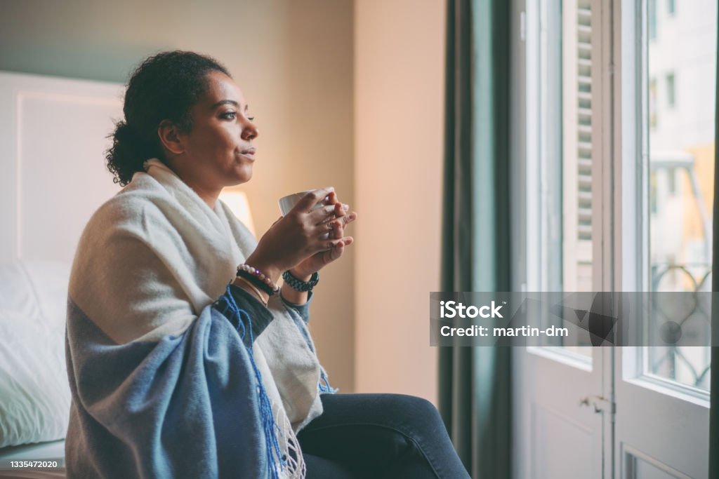COVID-19 lockdown Woman staying home for safety during coronavirus pandemic, drinking hot tea and looking through the window Winter Stock Photo