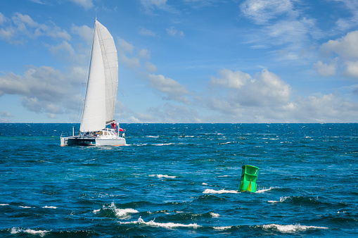 A sleek white double hulled catamaran with sails extended cruises  west towards the Cape Cod Canal on an August afternoon.